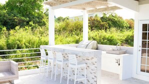 An outdoor patio with a marble bar, white chairs, and a seating area with a sofa and a sink. - Charming 2-bedroom villa with AC, WiFi in tranquil Osbourn-Fitches Creek  (St. Georges)