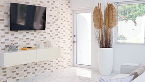 A modern living room with a white sofa, a large flat-screen TV mounted on a brick-patterned wall, a white console table, and a large vase with dried plants. - Charming 2-bedroom villa with AC, WiFi in tranquil Osbourn-Fitches Creek  (St. Georges)