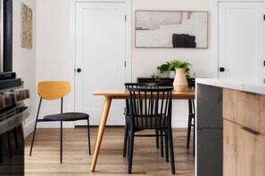 A dining area with a wooden table, two chairs, a potted plant, and a painting on the wall.
