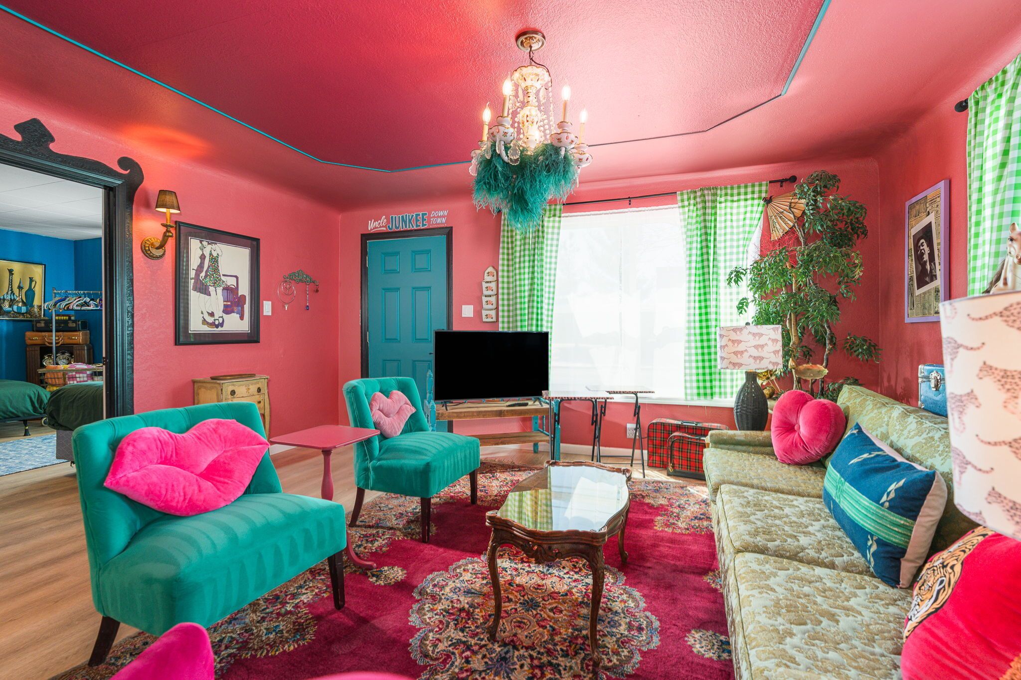 Un salon lumineux et accueillant, avec des meubles aux couleurs turquoise et rouge, un lustre et un téléviseur.