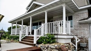 A two-story house with a covered porch, stone foundation, and a small garden area. - Copper Crown Retreat with Lake Superior Views (Bayfield)