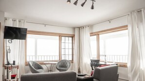 A modern living room with a flat-screen TV, two armchairs, a small table, and a balcony with white curtains. - Copper Crown Retreat with Lake Superior Views (Bayfield)