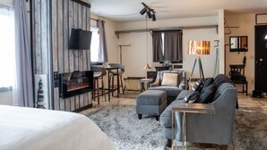 A modern hotel room with a bed, a sofa, a TV, a fireplace, and a dining area. - Copper Crown Retreat with Lake Superior Views (Bayfield)