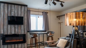 A modern living room with a fireplace, a TV mounted on a wooden wall, a dining area with chairs, and a sofa. - Copper Crown Retreat with Lake Superior Views (Bayfield)