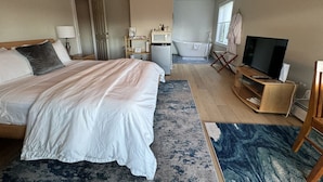 Een hotelkamer met een groot bed, een televisie, een bureau, een stoel, een badkamer en een douche.