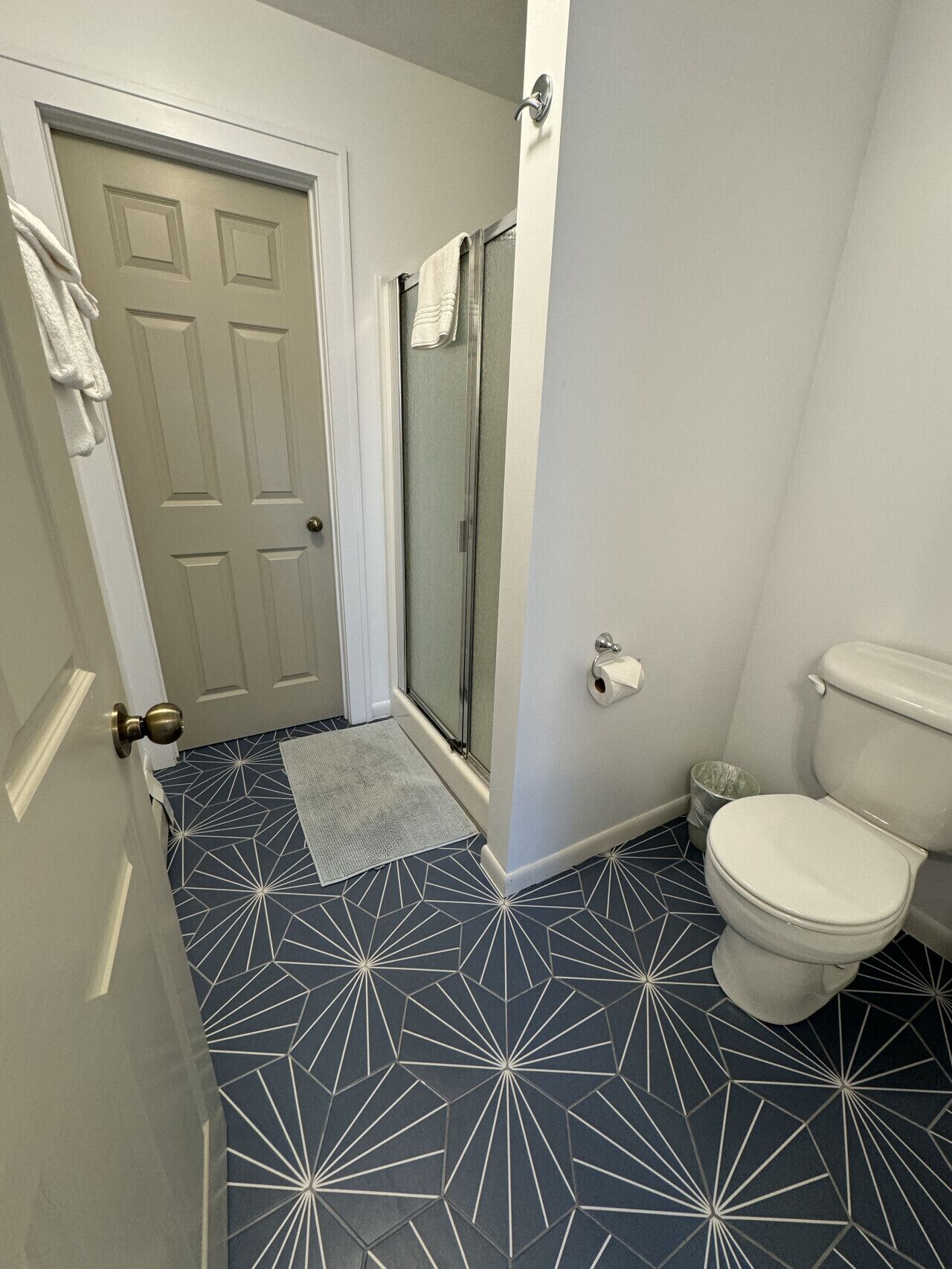 Une salle de bain avec un carrelage au motif géométrique, des toilettes, une douche avec une porte en verre et une serviette accrochée à la porte.