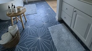 Een moderne badkamer met een vrijstaand bad, een houten kruk met toiletartikelen, en een groot raam met uitzicht op bomen.