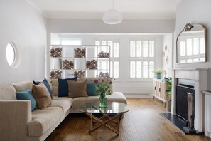 En moderne stue med en beige sofa, et sofabord i glas og en pejs.
