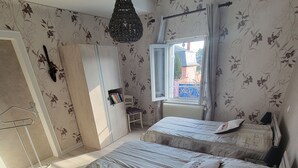 Une chambre avec deux lits, un radiateur, une fenêtre avec des rideaux, un luminaire suspendu et une bibliothèque.