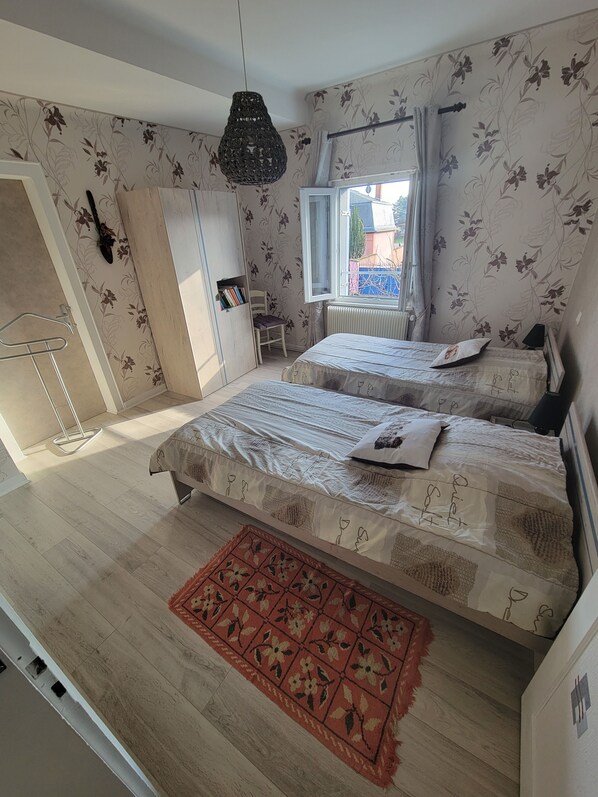 Un dormitorio con dos camas, un radiador, una ventana con cortinas, una lámpara colgante y una estantería.