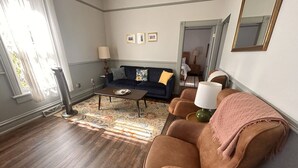 Ein Wohnzimmer mit dunklem Holzboden, einem blauen Sofa, einem braunen Sessel und einem gemusterten Teppich.