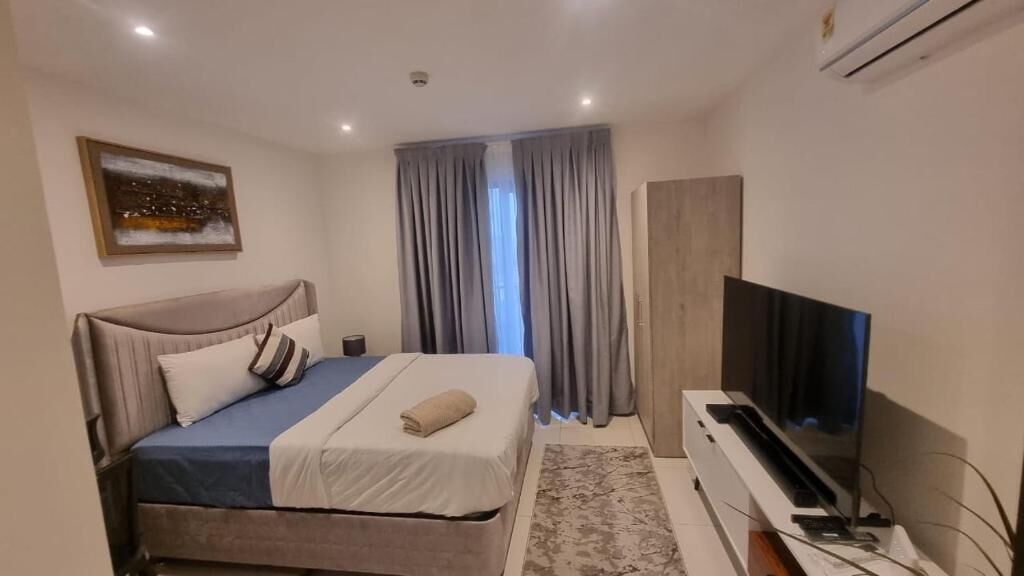 Un dormitorio moderno con una cama, un televisor y un amplio ventanal con cortinas.