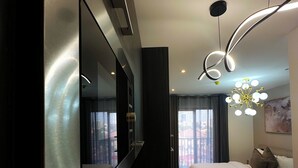 Une chambre d’hôtel moderne dotée d’un grand téléviseur à écran plat, d’un lit avec une literie blanche, d’un tapis à motifs et d’un lustre original.