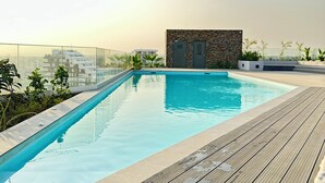 Une piscine sur le toit, dotée d’une terrasse en bois, entourée de verdure et d’un mur en pierre.