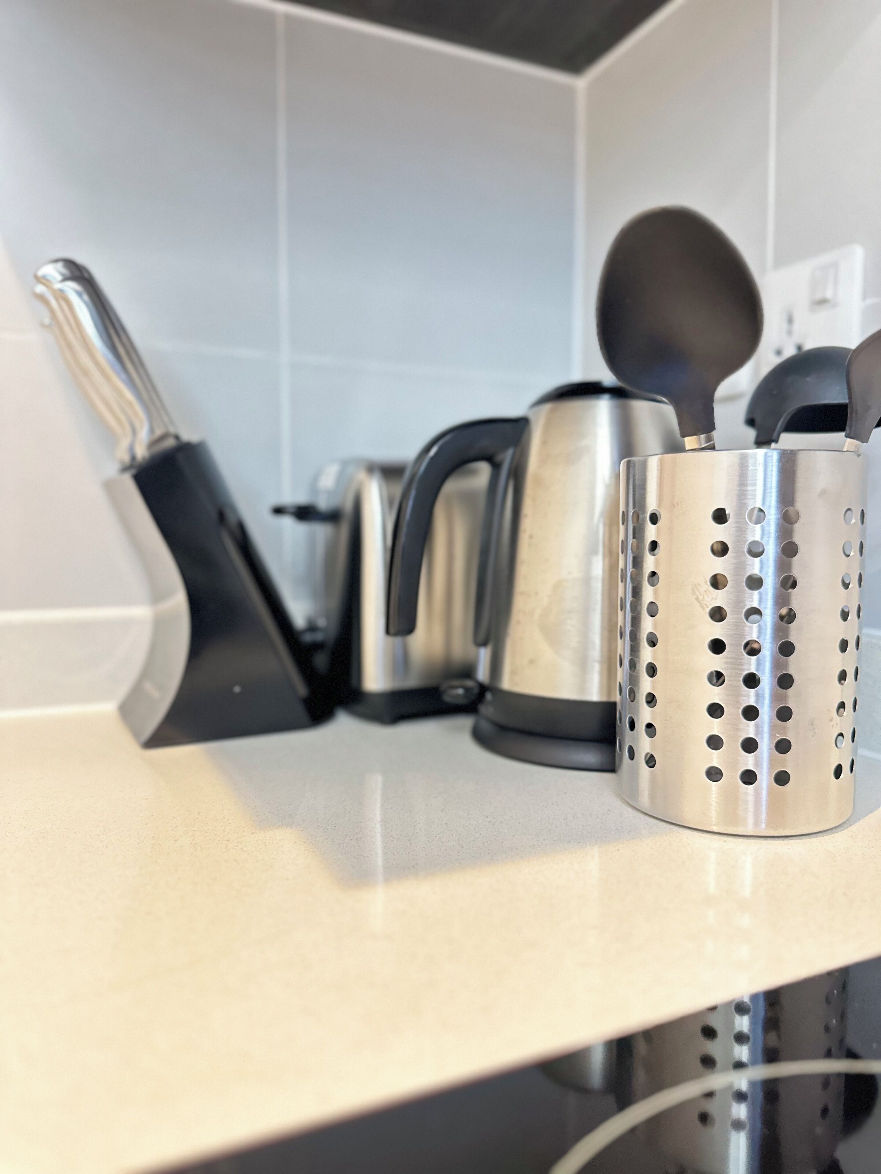 A kitchen counter with a kettle, a coffee maker, and a colander.