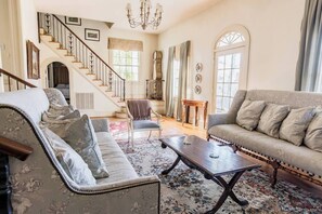 A spacious living room with a staircase, a sofa set, a coffee table, and a chandelier.