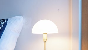 Une table de chevet avec une lampe, un tiroir, et un lit avec du linge de lit blanc.