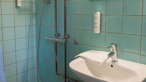 Une salle de bain avec des carreaux turquoise, un lavabo blanc et une douche équipée d’un pommeau de douche à main.