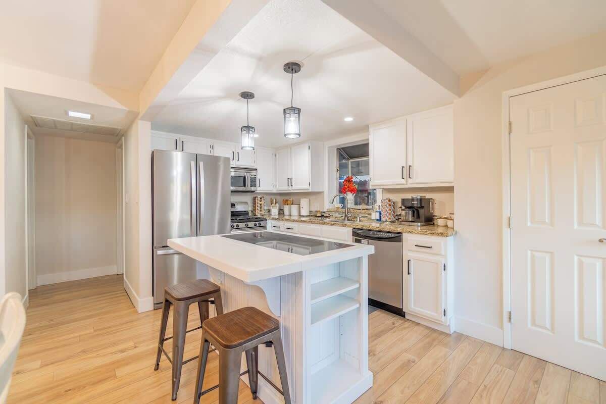 A modern kitchen with white cabinetry, stainless steel appliances, and a central island with stools.