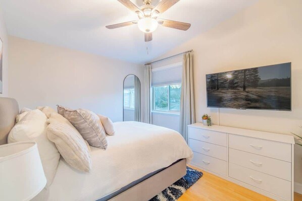 A bedroom with a bed, a ceiling fan, a window, a TV, and a dresser. - Modern Retreat | Game Room + Backyard Patio (Reno)