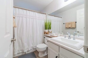 Een badkamer met een wit toilet, een wastafel met spiegel en een douchegordijn.