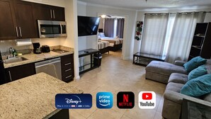 Una sala de estar moderna con una televisión de pantalla plana, un sofá y un comedor con cocina.
