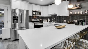 A modern kitchen with white cabinetry, stainless steel appliances, a large island, and pendant lighting. - Ultimate Coachella Stay: Pool & Fun & pickleball (Coachella)