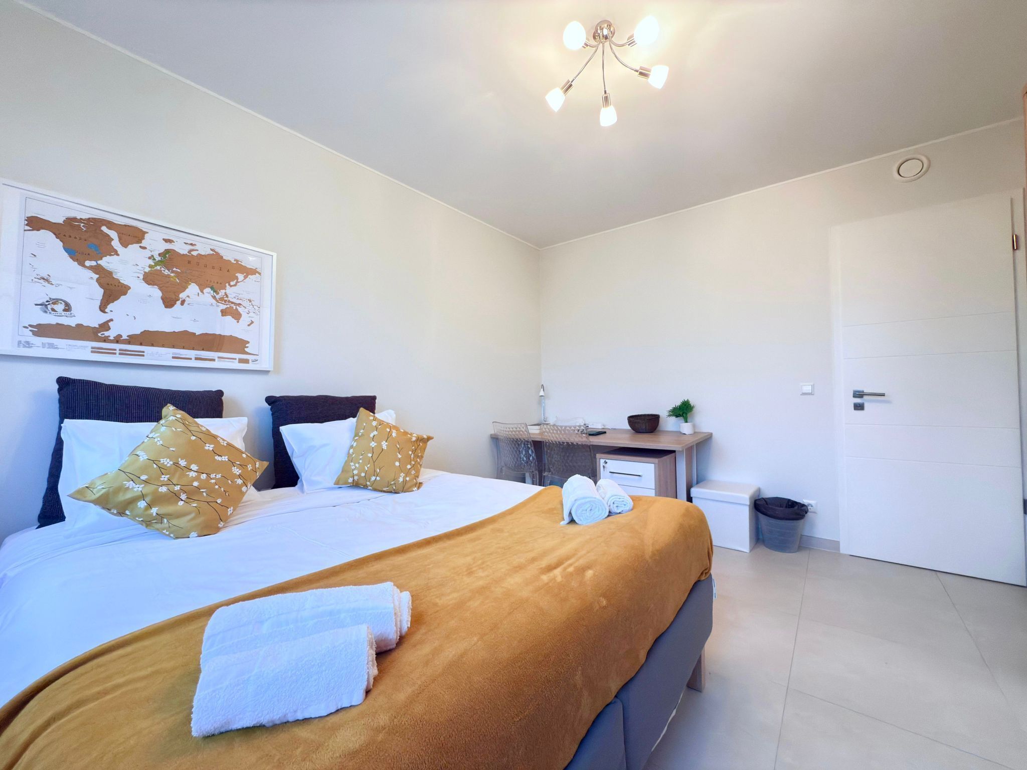A neatly arranged bedroom with a bed, pillows, a desk, and a map on the wall.