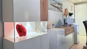 A modern kitchen with white cabinetry, a wooden accent wall, a glass display case with a red sculpture, and a microwave on the counter. - Comfort 2 bedrooms Apt w balcony&parking (Mamer)