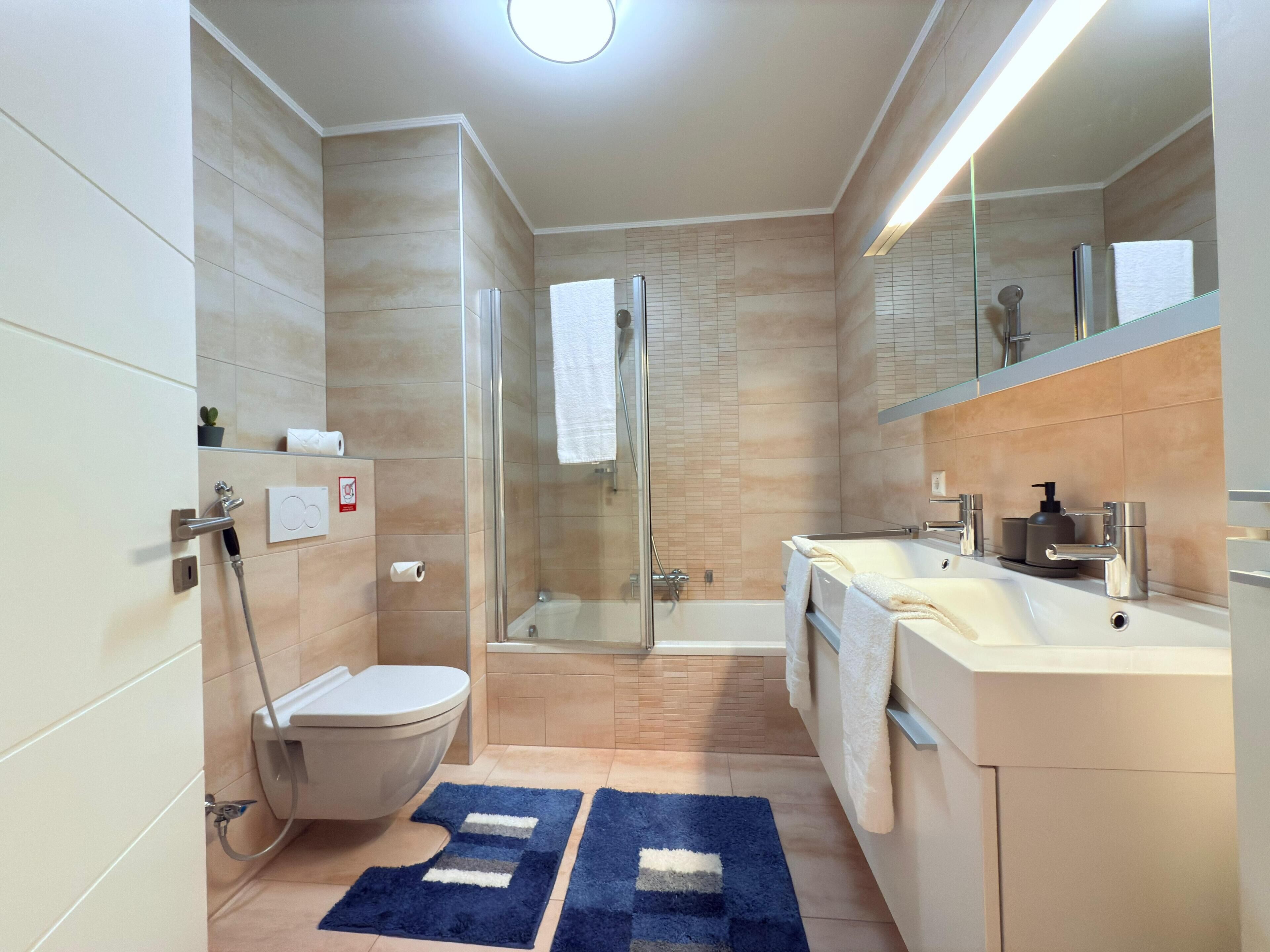 Un baño moderno con cabina de ducha de vidrio, inodoro, bañera y lavamanos con espejo.