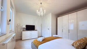 A bedroom with a bed, a dresser, a television, a chandelier, and a wardrobe. - Comfort 2 bedrooms Apt w balcony&parking (Mamer)
