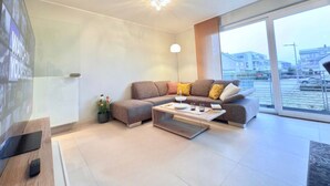 A modern living room with a sofa, coffee table, and a large window offering a view of the city. - Comfort 2 bedrooms Apt w balcony&parking (Mamer)