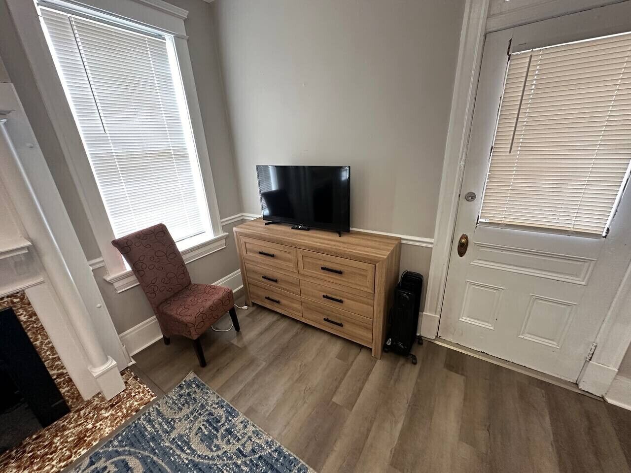 A room with a wooden dresser, a television on top, a patterned chair, and a door with a window.