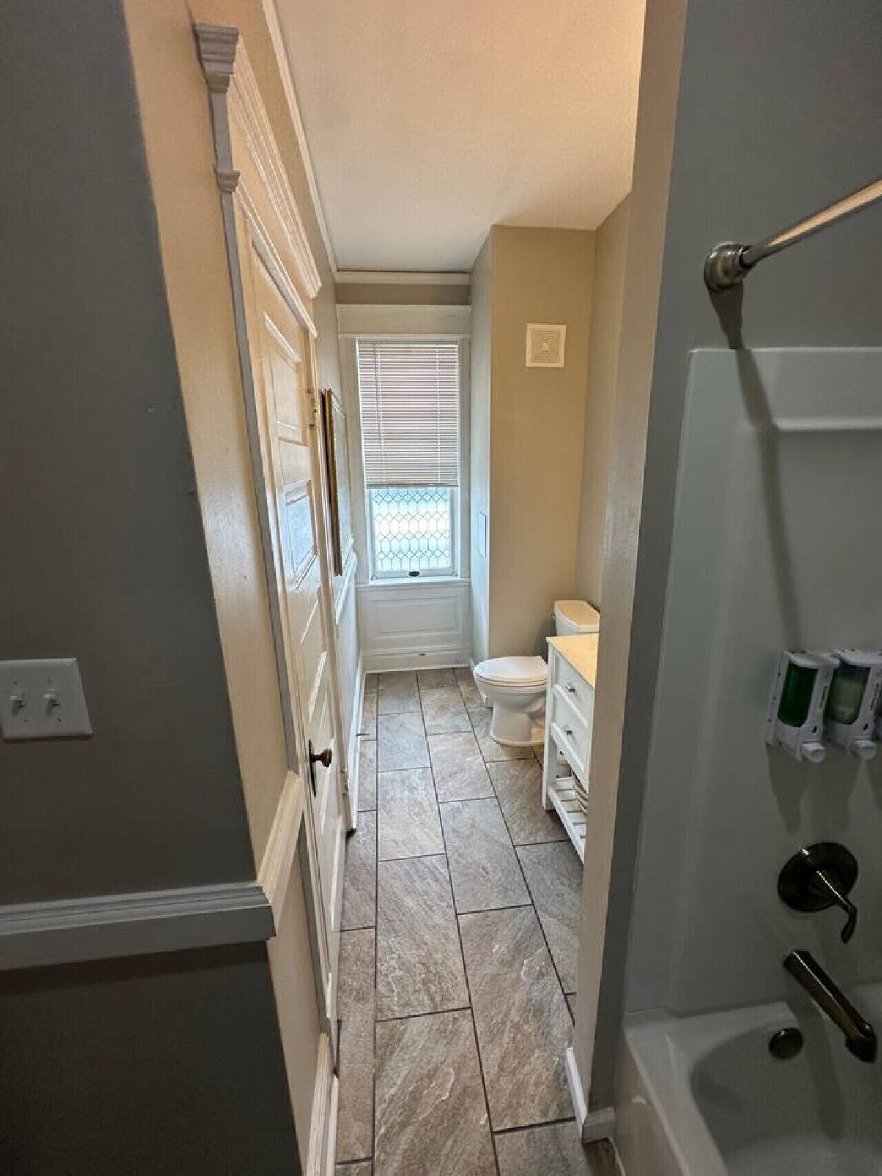 A narrow hallway with a bathroom on the right, featuring a toilet, sink, and a shower area.