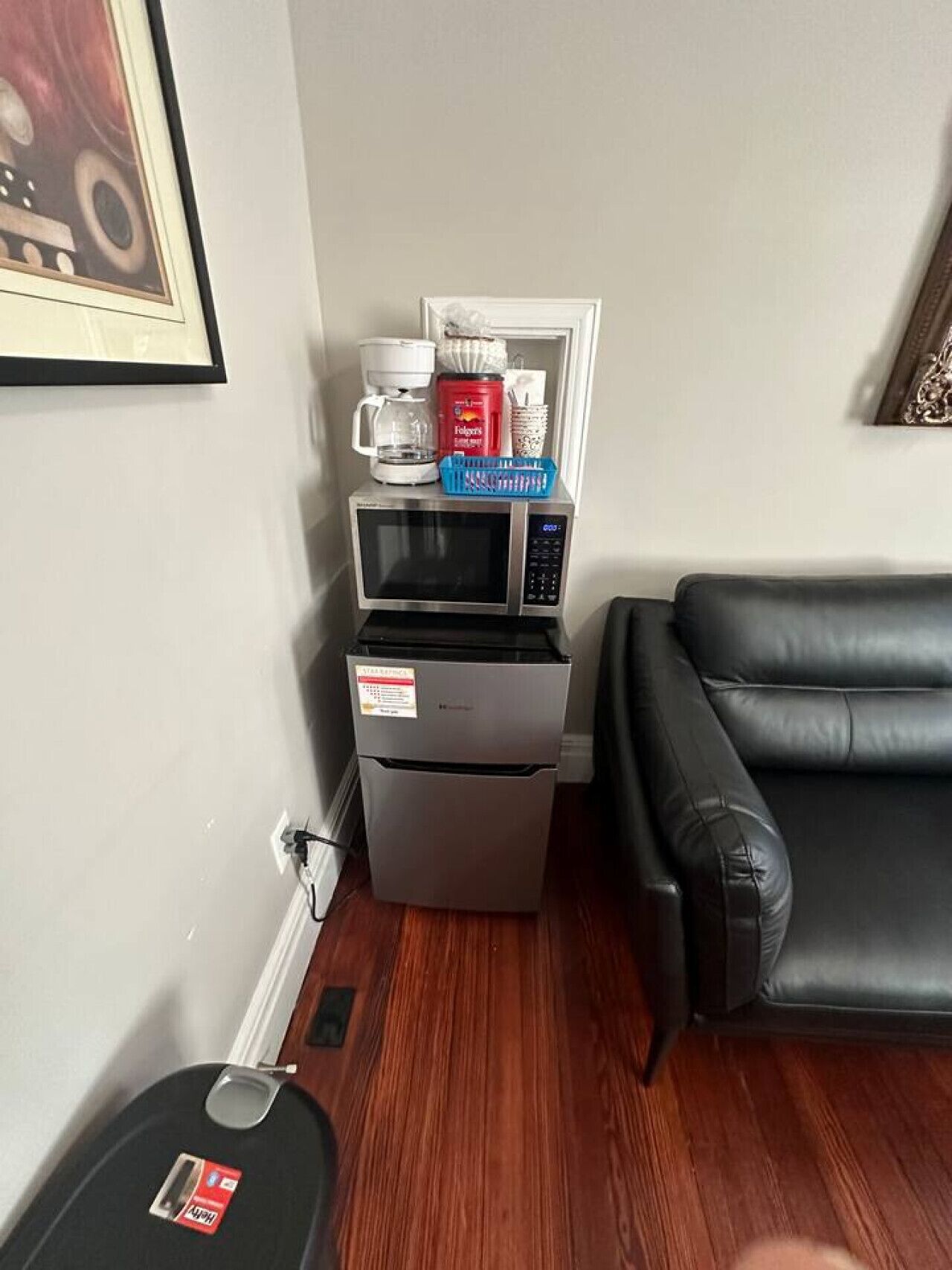 A compact kitchenette with a microwave, coffee maker, and storage containers. A black leather sofa is visible to the right.