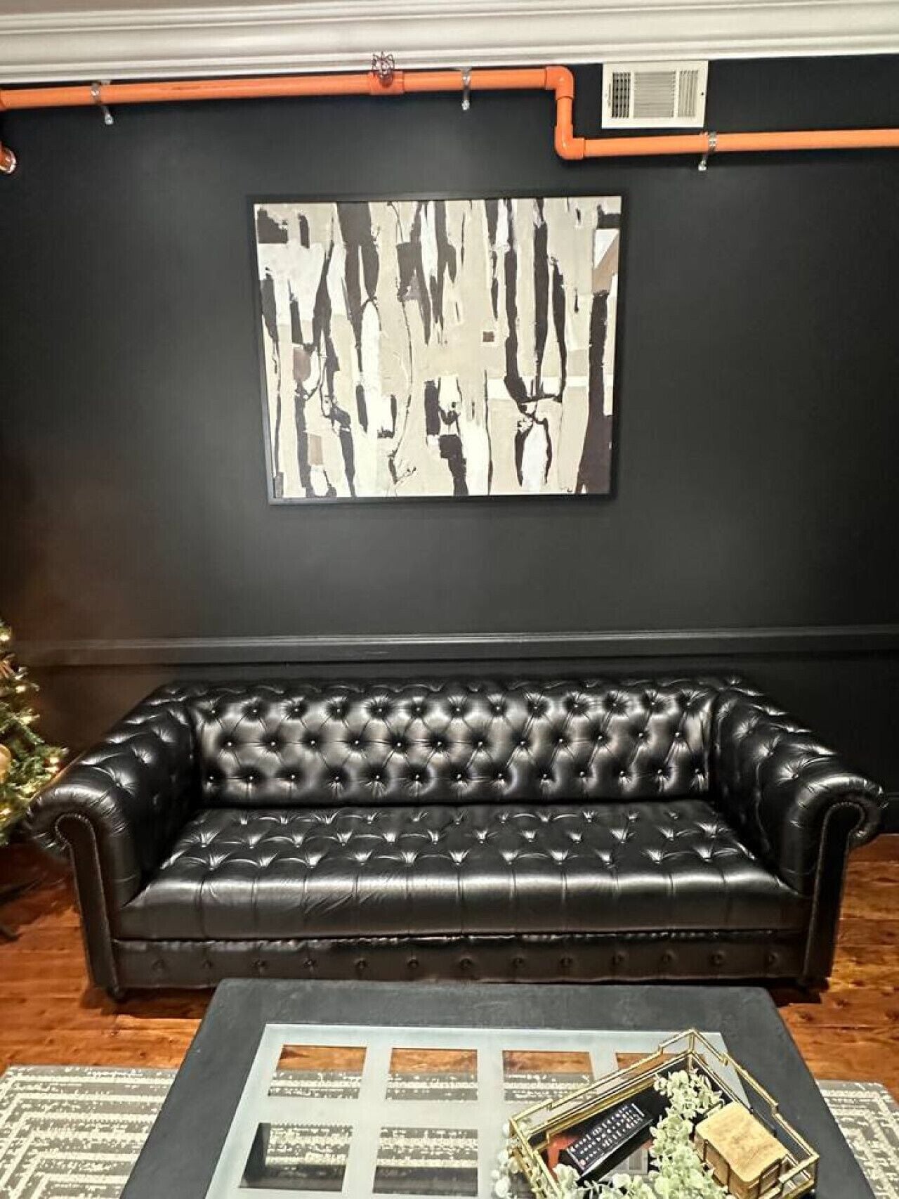A black leather sofa in a room with a black wall and a large abstract painting.