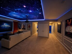 Sala de cine en casa con techo estrellado, un televisor de pantalla plana grande y un área de descanso.