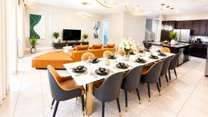 Een moderne eetruimte met een lange tafel, stoelen en een televisie op de achtergrond.