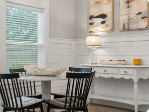 A dining area with a white table and chairs, a lamp, and abstract art on the wall. - Beachumall/Golf Cart/Bikes/Walk to Beach (Santa Rosa Beach)