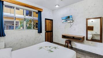 Habitación de hotel con cama, banca de madera, televisor, espejo y ventana con cortinas.