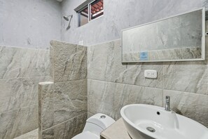 A bathroom with a marble wall, a large mirror, a sink, and a shower. - Hotel Tamarindo INN (Tamarindo)