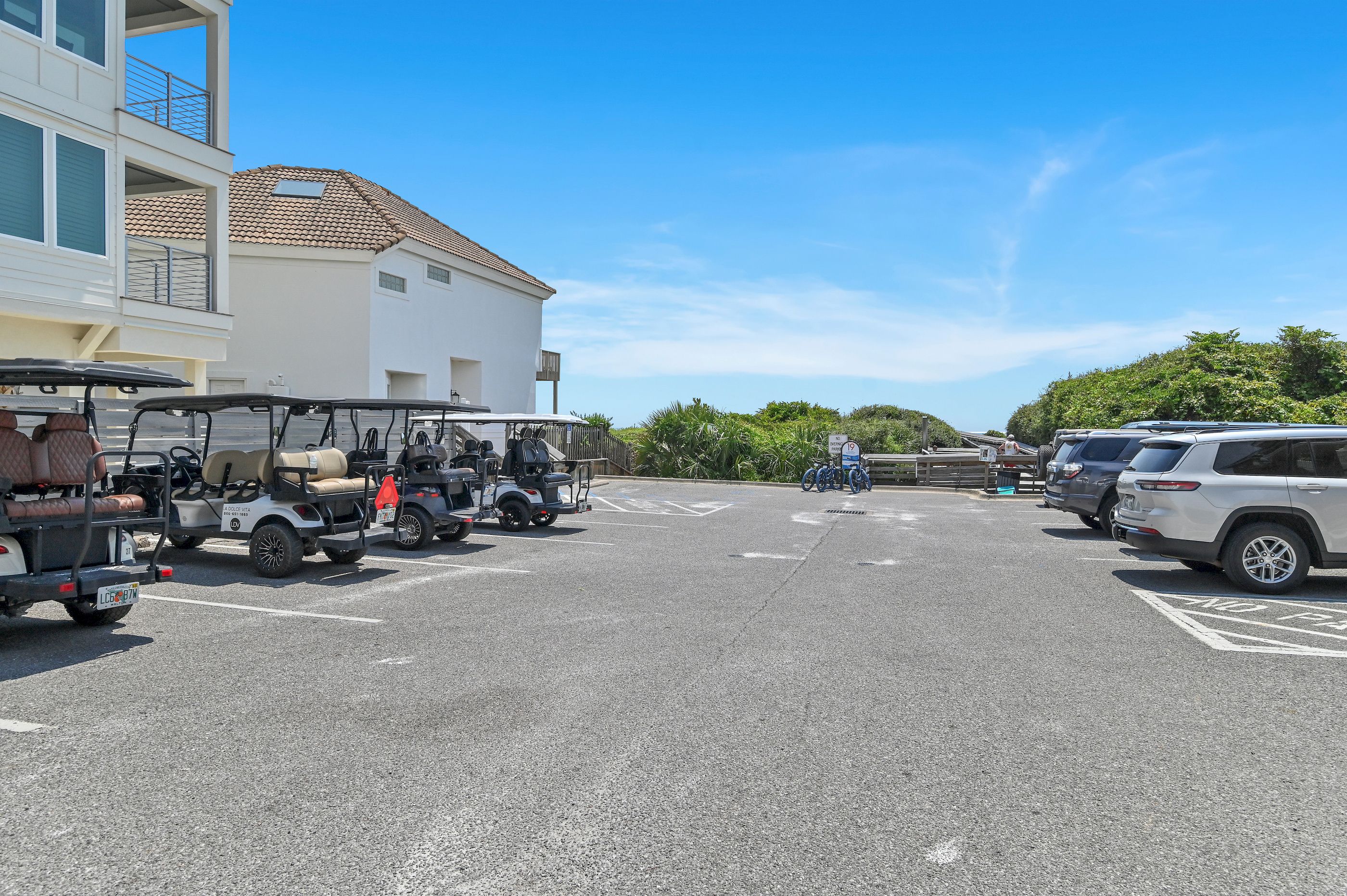 Un parking où sont garés des voiturettes de golf et un bâtiment blanc avec un toit recouvert de tuiles.
