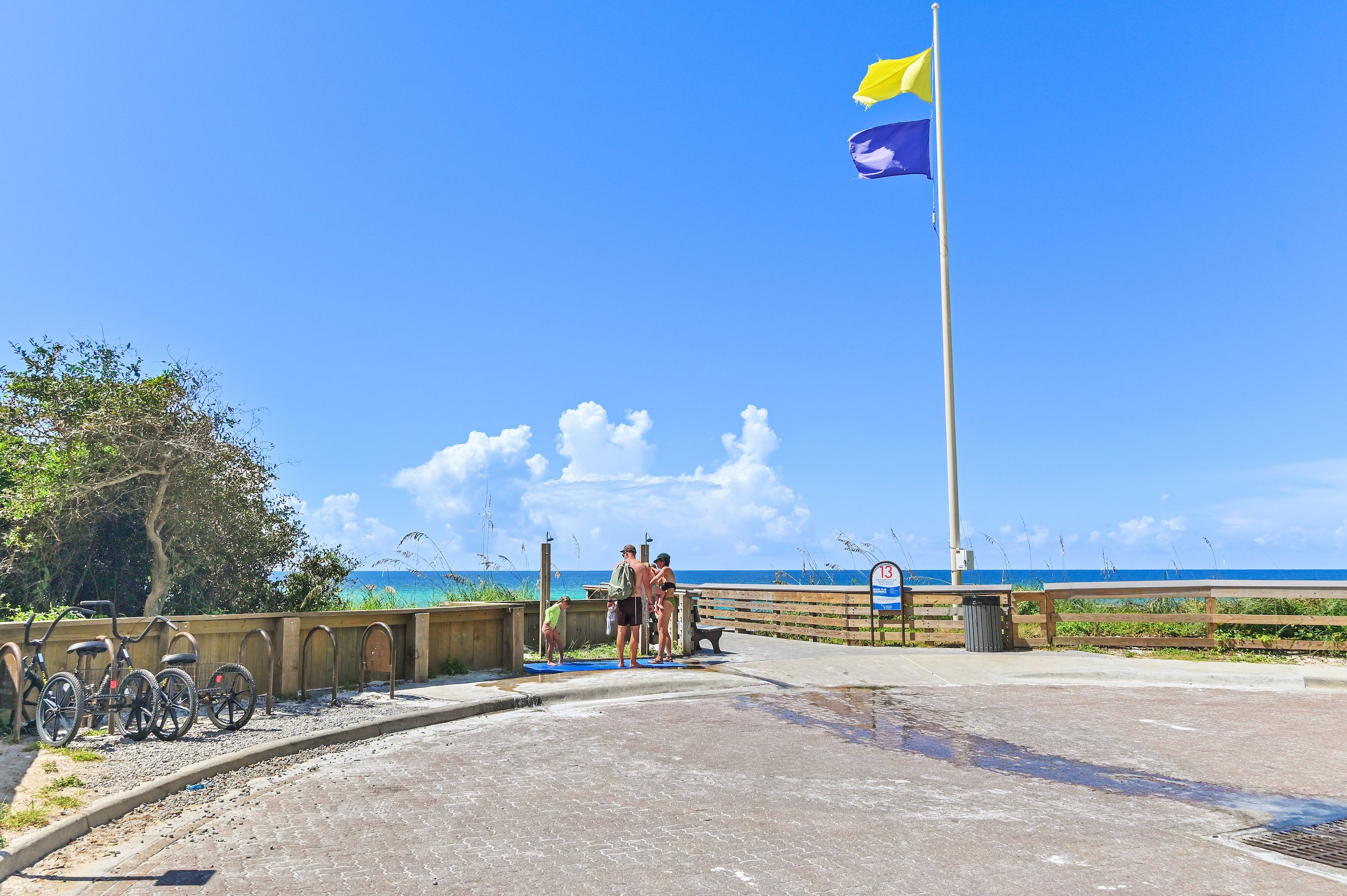 A coastal walkway with a flag, a wooden fence, and a clear view of the ocean.