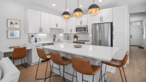 A modern kitchen with white cabinets, a large island with bar stools, stainless steel appliances, and pendant lighting. - VitaSea/Private Beach/Bike2Seaside (Santa Rosa Beach)