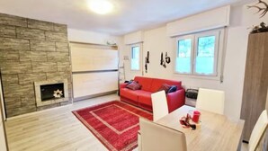 A modern living room with a fireplace, red sofa, dining table, and a red rug. - Elegant Apartment in the center of Aprica, very close to the ski slopes (Aprica)