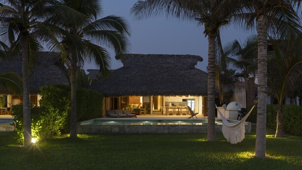 A resort with a pool, thatched-roof structures, and palm trees.