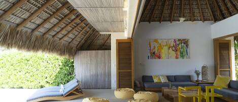 Una habitación con techo de paja, un sofá azul y pufs.