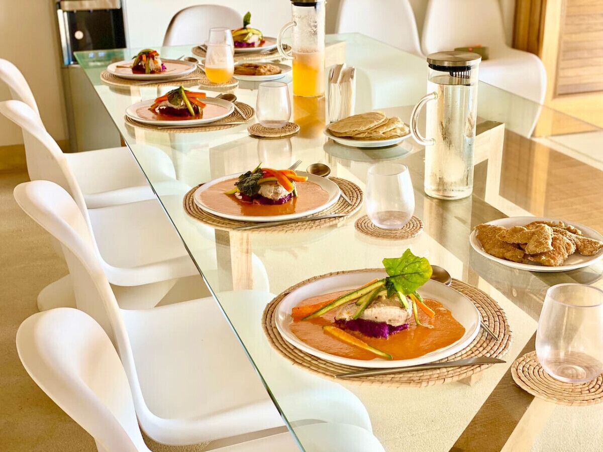 Une table à manger dressée avec des assiettes remplies de nourriture, des verres et une carafe de jus d’orange.