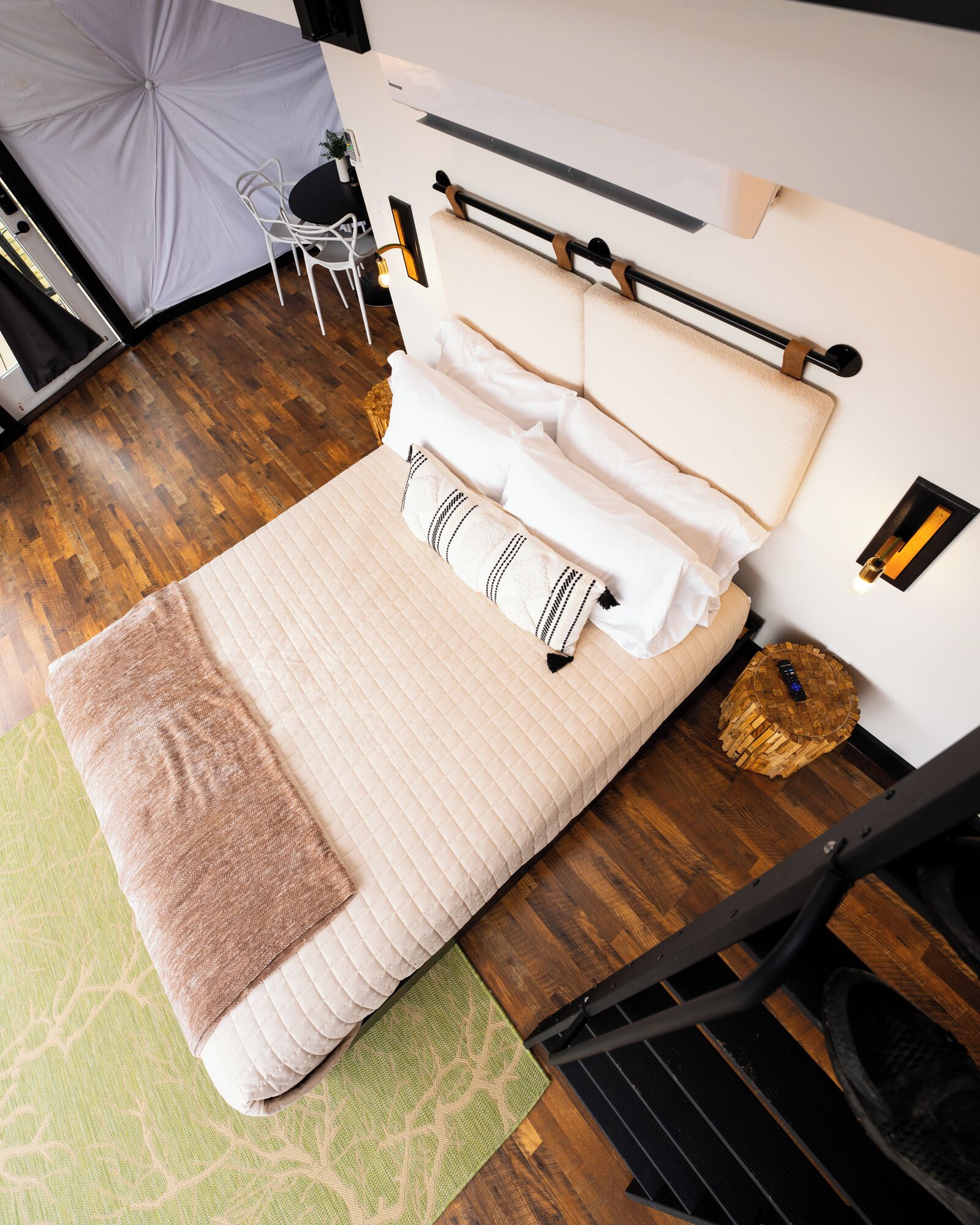 Una camera da letto ordinata con un letto, cuscini, un comodino e una piccola sedia.