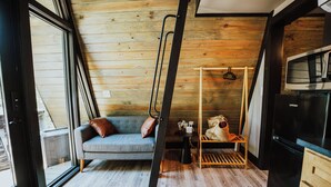 A cozy room with a sofa, a hanging chair, a small table with a vase, and a refrigerator. - Modern A-Frame Cabin: Hot Tub, TV, & Lake Views (Cedar Bluff)